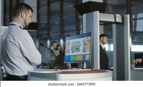 Hombre uniformado parado en el mostrador del punto de control y mirando el monitor con rayos X del equipaje.