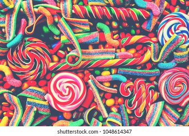 Coloridos y variados bastones de caramelo y piruletas espirales de colores del arco iris con mermelada dispersa, gominolas y dulces redondos de diferentes colores. Vista superior. Fondo de caramelo