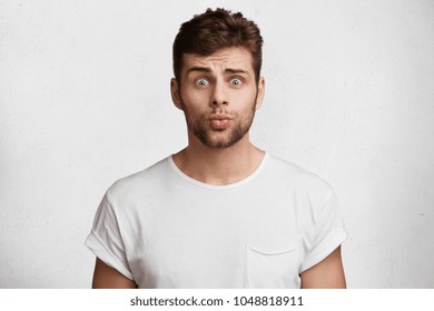無邪気な表情をした魅力的な若い無精ひげを生やした男性の写真。青い目と丸い唇でカメラに映り、ガールフレンドに許しを請い、白い背景に罪悪感を抱いている。
