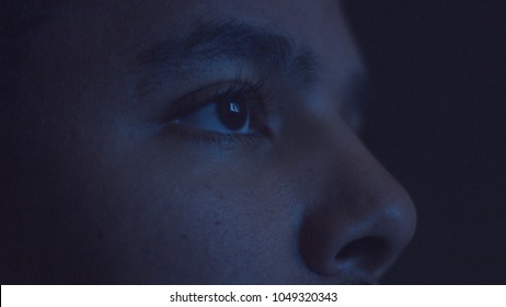 Hombre de raza mixta viendo televisión en la oscuridad con luz de color diferente a la televisión en la cara. Primer plano de los ojos