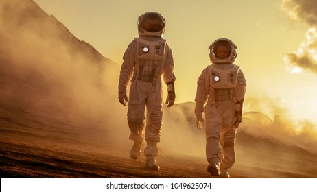 Two Astronauts in Space Suits Confidently Walking on Mars, Exploration Expedition on the Planet's Surface. Red Planet Covered in Rocks, Gas and Smoke. Humans Overcoming Difficulties.