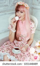 밝은 방에서 분홍색 드레스를 입은 아름다운 젊은 여성 인형이 안락의자에 앉아 찻잔과 차를 마시는 모습, 티파티, 로리타. 일본 거리 패션.