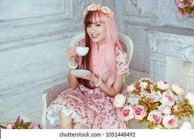 분홍색 드레스를 입은 아름다운 젊은 여성 인형, 밝은 방과 꽃, 컵이 있는 의자에 앉아 있는 티파티, 로리타. 일본 거리 패션. 초상화.