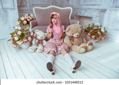 꽃이 있는 방에서 분홍색 드레스를 입은 아름다운 젊은 여성 인형이 바닥에 앉아 장난감과 봉제 곰, 로리타를 가지고 있습니다. 그의 손에는 데레가 있습니다.