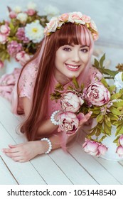 분홍색 드레스를 입은 아름다운 젊은 여성 인형이 밝은 방과 꽃 속에 바닥에 누워 있습니다, 로리타. 일본 거리 패션. 초상화.