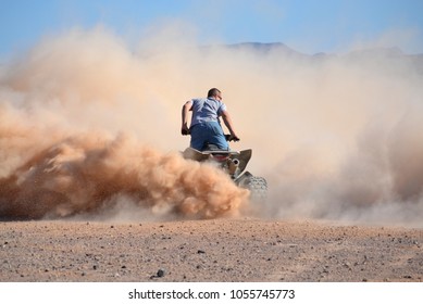 Male rider on quad in dust cloud in desert