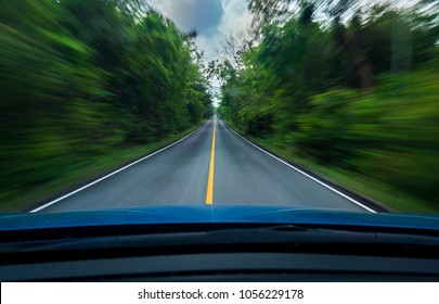 Vooraanzicht van blauwe auto rijden met hoge snelheid op het midden van de asfaltweg met witte en gele lijn van verkeerssymbool in het groene bos. Bomen naast de weg zijn wazig. Auto met wazige beweging.