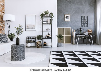 Plant on metal table in open space interior with poster and work area against concrete wall