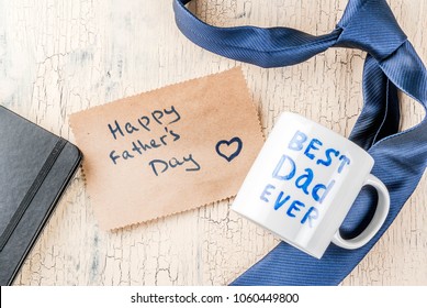 Father's Day gift concept, greeting card background, gift box, tie decoration, mug with inscription Best Dad Ever, notebook, top view