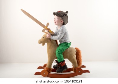 Funny child in old military cap with red star, on toy horse-rocking horse with wooden sword. Boy dreams of battles, victories and adventures. Concept training of spirit, education morale, patriotizm