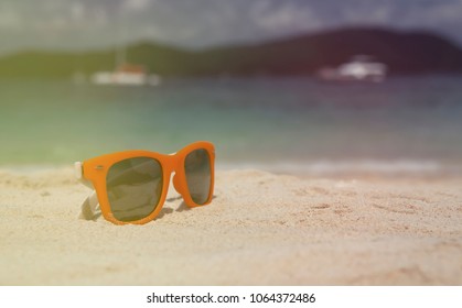 Travel and vacation concept. with copy space Bright orange sunglasses on the white sand of a tropical beach. Vintage look.