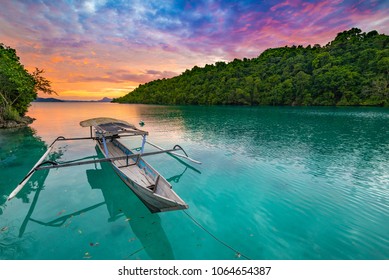 トギアン諸島インドネシア、カリブ海に沈む夕陽、劇的な空、トゲアン諸島の青緑色のラグーンに浮かぶ伝統的なボート、スラウェシ、インドネシアの旅行先。