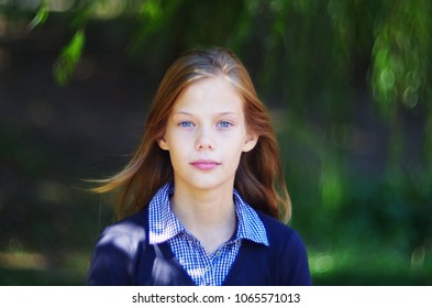Nahaufnahmeporträt eines Teenager-Mädchens mit strahlend blauen Augen und heller Haut. Draußen Porträt eines jugendlich Mädchens auf einem hellen, sonnigen, grünen, unscharfen Hintergrund