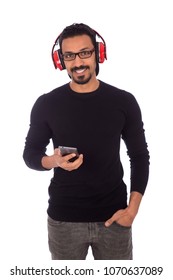 Jonge smiley man die hand in de zak staat en zijn telefoon vasthoudt en een rode koptelefoon op het hoofd zet, luisterend naar muziek, geïsoleerd op een witte achtergrond.