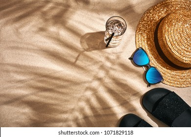 Sandaal, strohoed en zonnebril op een zanderige achtergrond, bovenaanzicht