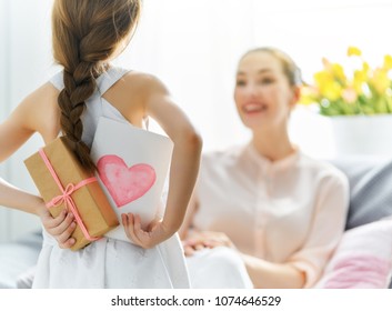 Alles Gute zum Tag der Frauen! Kindertochter gratuliert Mutter und gibt ihr Postkarte und Geschenk. Mama und Mädchen lächeln und umarmen sich. Familienurlaub und Zweisamkeit.