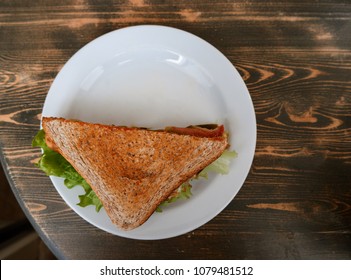 Sandwich panggang dengan ham, keju, dan sayuran di piring di atas meja kayu.