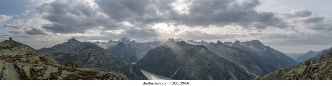 Panoramablick auf den Grimselsee in den Schweizer Alpen mit dramatischen Sonnenstrahlen, die durch die Wolken brechen