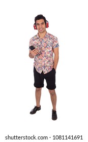 Full-length shot van een jonge smiley man die hand in de zak staat en zijn telefoon vasthoudt en een rode koptelefoon op het hoofd zet terwijl hij naar muziek luistert, geïsoleerd op een witte achtergrond.