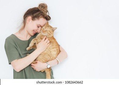 Closeup retrato guapo joven hipster mujer, abraza a su buen amigo jengibre gato sobre fondo de pared blanca. Emociones humanas positivas, expresión facial, sentimientos. Personas y animales enamorados.