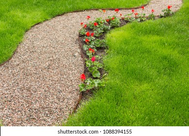 voetpad van klein grind in de tuin, langs het bloembed met rode bloemen, groen gras, selectieve focus