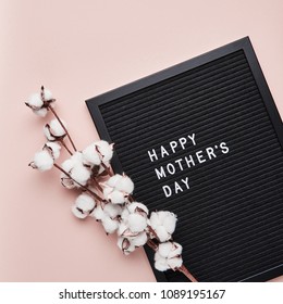 Black letterboard with white plastic letters with quote Happy Mother's Day, and cotton on pink background. Square crop.