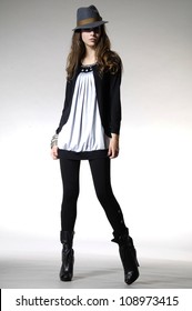 Full length attractive young fashion model in hat posing in light background