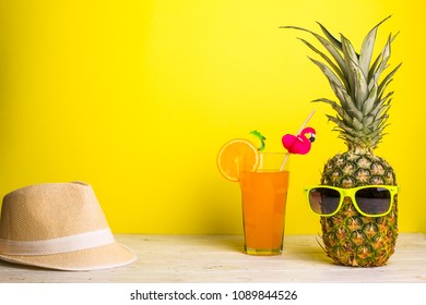 Zomer heldere compositie van modieuze ananas met zonnebril, strohoed en limonade met sinaasappel en mooie tubule versierd met flamingo op gele achtergrond
