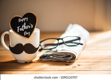 幸せな父の日のコンセプトです。黒い紙の口ひげを持つコーヒー カップ、幸せな父の日のテキストと新聞、木製のテーブルの背景にメガネのハート タグ。
