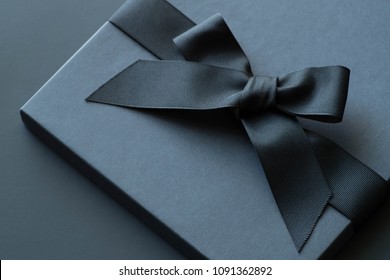 Caja de regalo negra sobre fondo oscuro contrastante, decorada con un lazo texturizado y plumas, creando un ambiente romántico. Ideal para cumpleaños, regalos de aniversario, tarjetas de regalo y postales.
