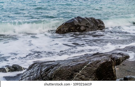 Pedras molhadas do mar na areia na maré baixa. Ondas e espuma do mar.