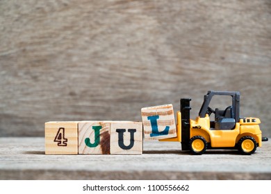 Forklift mainan menahan blok l untuk menyelesaikan kata 4 jul dengan latar belakang kayu (Konsep untuk tanggal kalender di bulan Juli)