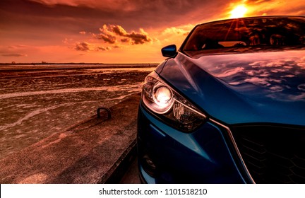 スポーツとモダンなデザインの青いコンパクト SUV 車は、日没時に海沿いのコンクリート道路に駐車。環境にやさしい技術。ビジネスの成功のコンセプト。ヘッドランプ ライトが開いている車。