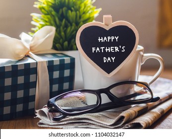 Glückliches Vatertagskonzept. Kaffeetasse mit Geschenkbox, Herzanhänger mit Happy Father's Day Text und Zeitung, Gläser auf Holztischhintergrund.