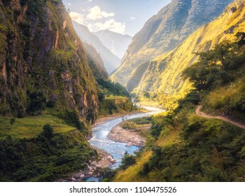 Colorful landscape with high Himalayan mountains, beautiful curving river, green forest, blue sky with clouds and yellow sunlight at sunset in summer in Nepal. Mountain valley. Travel in Himalayas