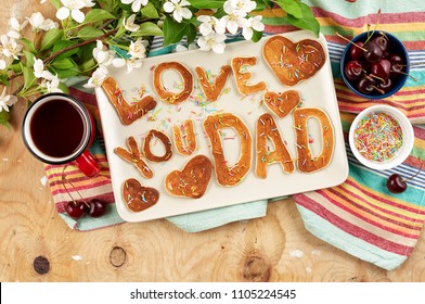 Special Father's Day breakfast. Alphabet Pancakes with sprinkles, cherries and cup of tea on wooden background with apple blossom branch. Closeup view