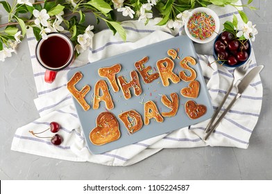 Special Father's Day breakfast. Alphabet Pancakes with sprinkles, cherries and cup of tea on a gray concrete background with apple blossom branch. Closeup view