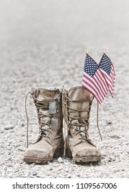 Old military combat boots with dog tags and two small American flags. Rocky gravel background with copy space. Memorial Day or Veterans day concept. Vintage tone.