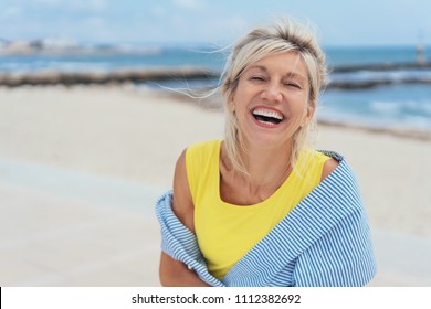 Lachende lebhafte blonde Frau mit einem Sinn für Humor, die auf einem tropischen Strand mit Kopienraum steht