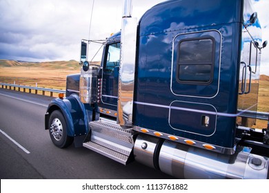 Dunkelblauer glänzender klassischer amerikanischer Sattelschlepper mit Chromzubehör mit Reflexion auf der Fahrerhausoberfläche, die auf der Straße mit gelbem Sommerfeld auf Hintergrund in Kalifornien läuft