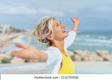 Freudige Frau, die die Freiheit des Strandes genießt, der mit offenen Armen und einem glücklichen Lächeln steht, das zum Himmel aufblickt