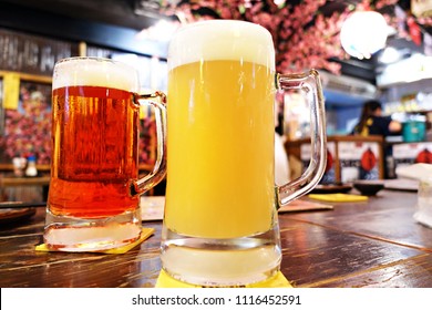 Two glass of a mug of beer, fruit beer and draft beer, put on the wood table in japanese resturant izakaya style, background is a sakura flower, fell like in japan, after work relax time.