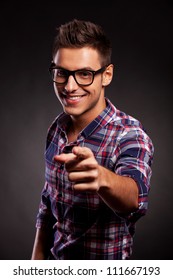 Foto van een jonge casual man met een bril die op de camera wijst, op een zwarte achtergrond