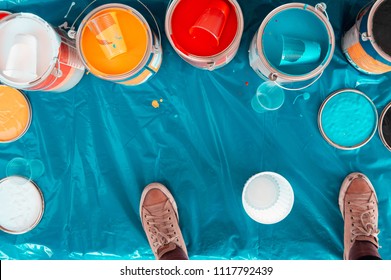 Vista superior de muchos cubos y contenedores de pintura de colores sobre una superficie de plástico turquesa y un par de zapatos marrones