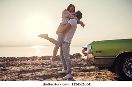 يقف زوجان رومانسيان بالقرب من سيارة قديمة خضراء على الشاطئ. رجل وسيم ملتح وامرأة شابة جذابة مع سيارة كلاسيكية عتيقة. قصة حب. سيارة عضلية