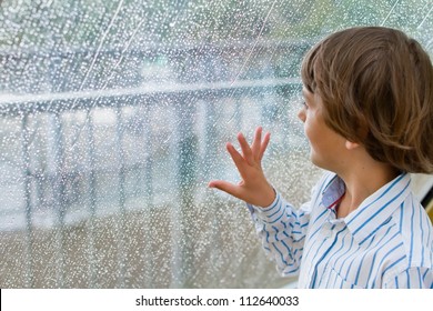 Niño sonriente mirando la lluvia afuera en una ventana