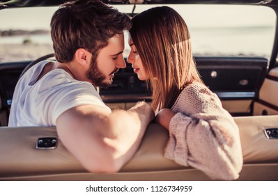 Una pareja romántica está sentada en un auto retro verde en la playa. Guapo hombre barbudo y atractiva mujer joven en coche clásico vintage. Historia de amor con estilo. Abrazarse y besarse estando en el coche.