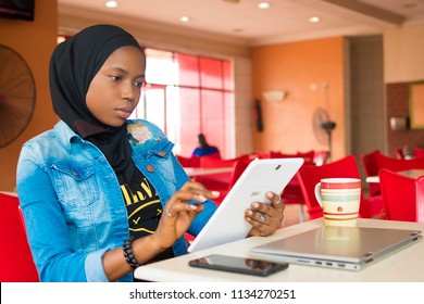 junges nigerianisches muslimisches Mädchen, das allein in einem Fast-Food-Restaurant mit ihrem Android-Tablet sitzt