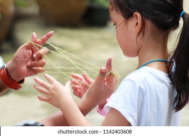 5-6 Jahre altes asiatisches kleines Mädchen, das mit ihrer Mutter Streicherspiel spielt. Hände, die Streicherspielkreativität spielen. Ein beliebtes Streicherspiel ist die Wiege der Katze oder die Wiege des Kaninchens.