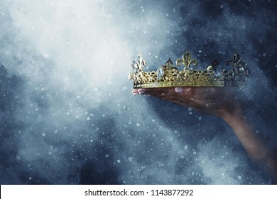 mysterieus en magisch beeld van de hand van de vrouw die een gouden kroon vasthoudt over gotische zwarte achtergrond. Middeleeuws periodeconcept